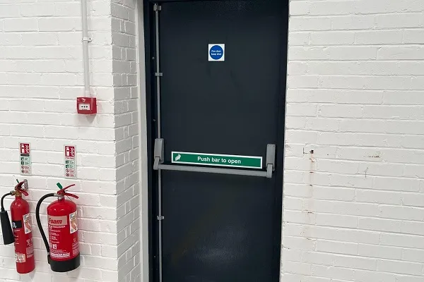 Commercial locksmith in Wellingborough fitting panic and emergency exit hardware to a steel door.