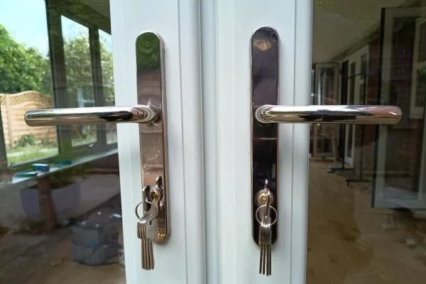 Keys in the locks of white uPVC French doors with chrome lever handles in Wellingborough.