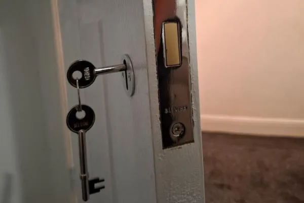 Silver mortice deadlock fitted to a white wooden internal door with keys inserted.