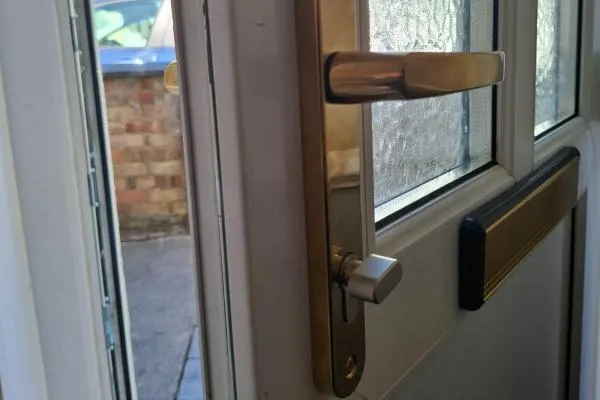 Brass lever door handle and thumbturn cylinder fitted to a white uPVC entrance door.