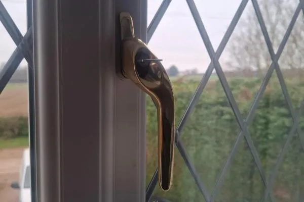 Gold locking window handle fitted to a white uPVC window with leaded glass, illustrating uPVC window repair services in Castle Ashby.
